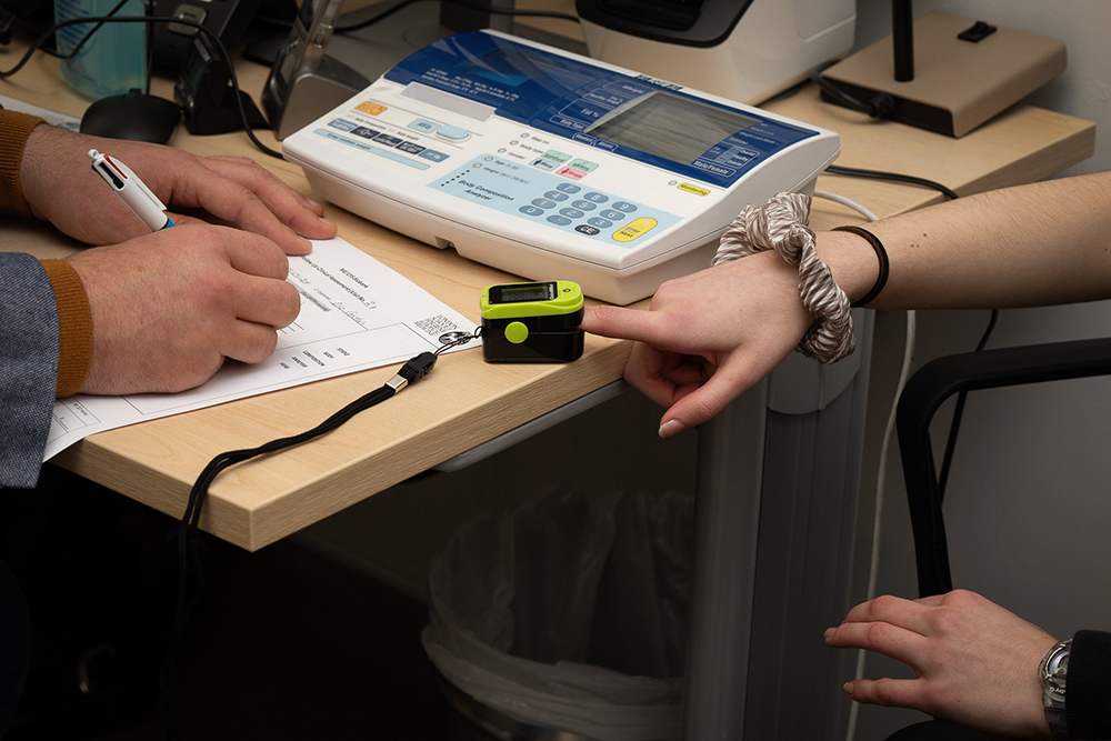 A girl has her finger in a heart rate reader as a doctor writes notes.